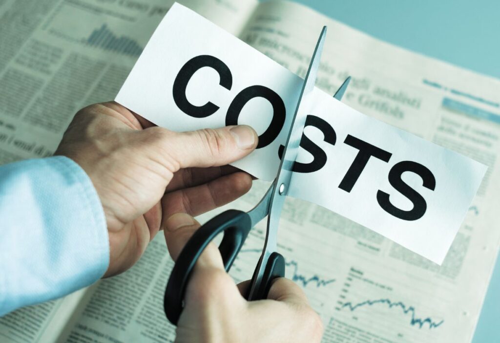 Person cutting a paper with "costs" written on it with a financial newspaper in the background